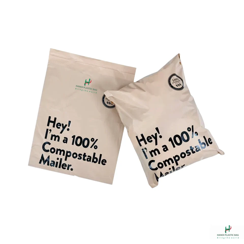 Two beige compostable mailers with bold black text reading 'Hey! I'm a 100% Compostable Mailer.' and small logo in corner; product branding visible (reusable packaging).